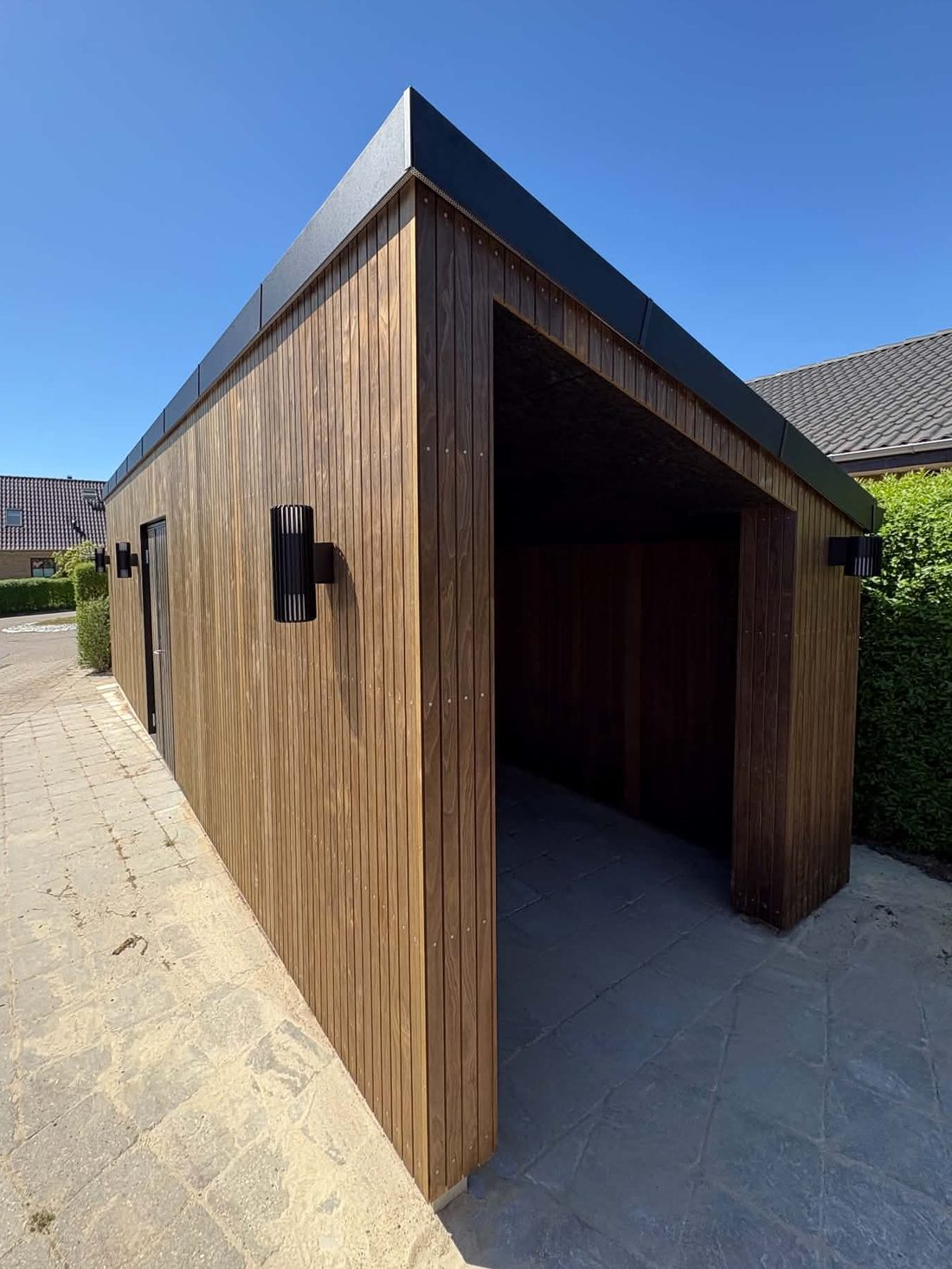 Carport og skur med lodret træbeklædning og sort tagkant